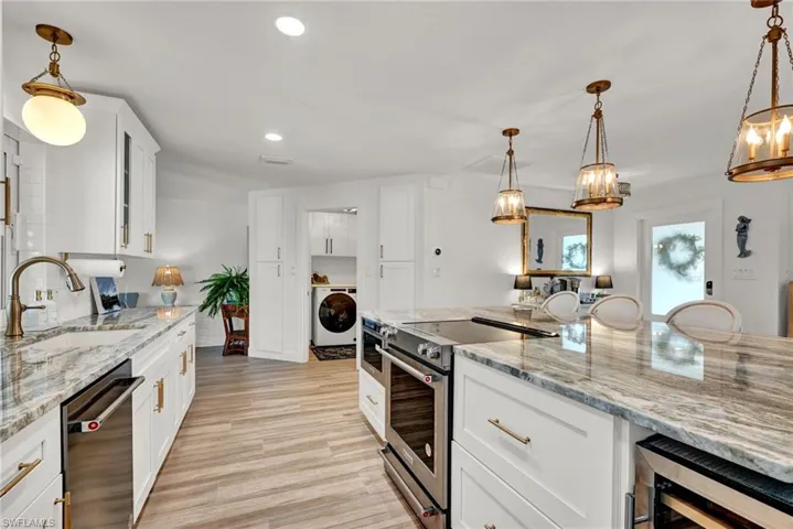 Kitchen featuring light wood-type flooring, dishwasher, stainless steel range with electric cooktop, microwave and wine cooler/large laundry room with washer and dryer and entrance to the oversized garage