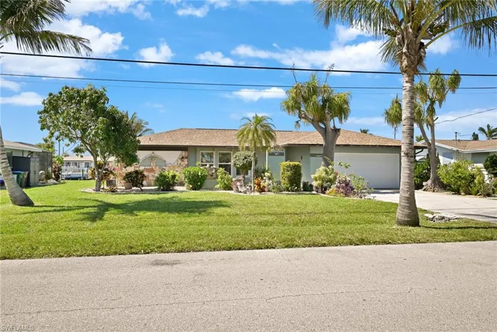 Ranch-style home with concrete driveway, an attached garage, a front yard, and stucco siding, mango tree and fig tree and lime tree