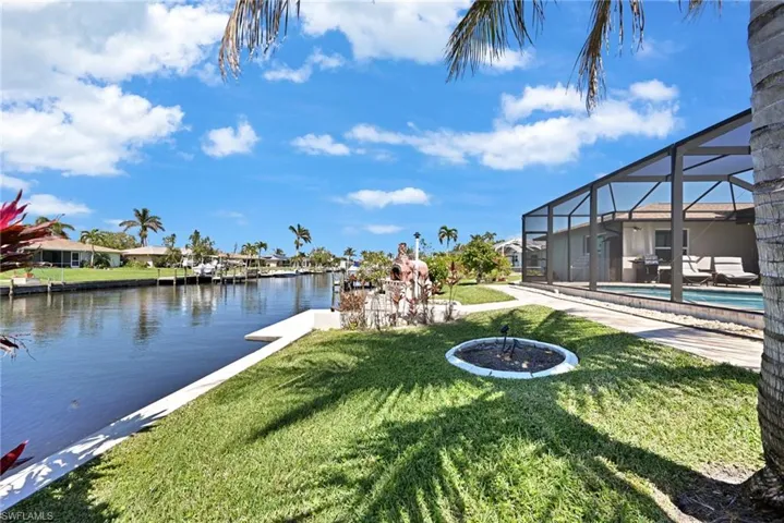 View of yard featuring a lanai, an outdoor pool, and a water view with lemon trees, 2 coconut palms, mango tree