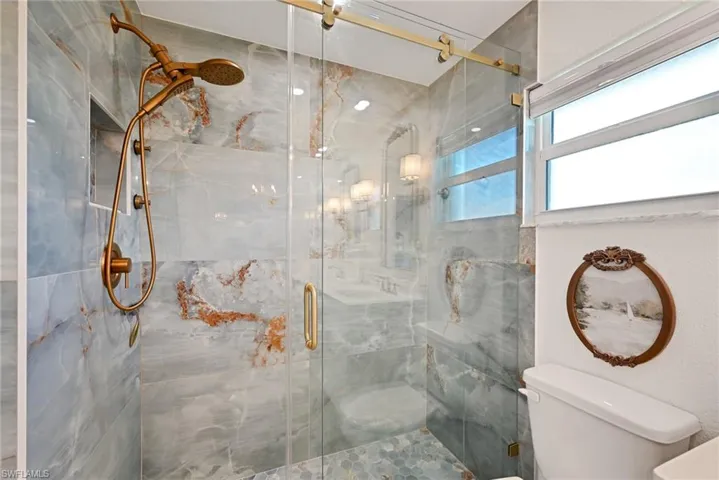 Full bath with a marble finish shower and toilet