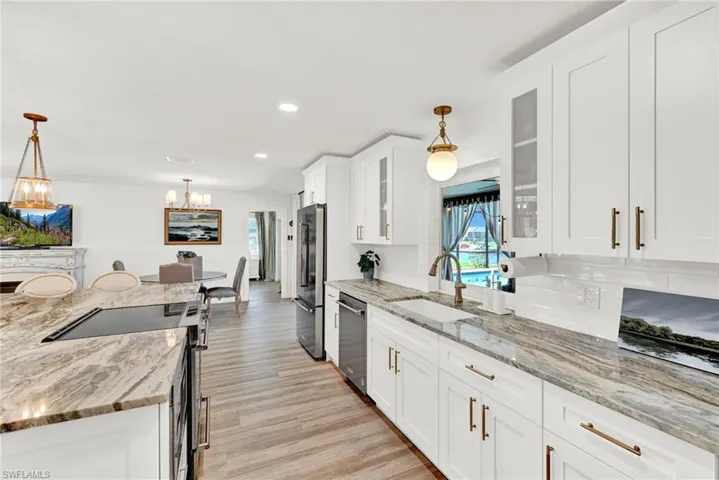 Kitchen with white cabinets, decorative light fixtures, appliances with stainless steel finishes, and large famers sink and quartz counters