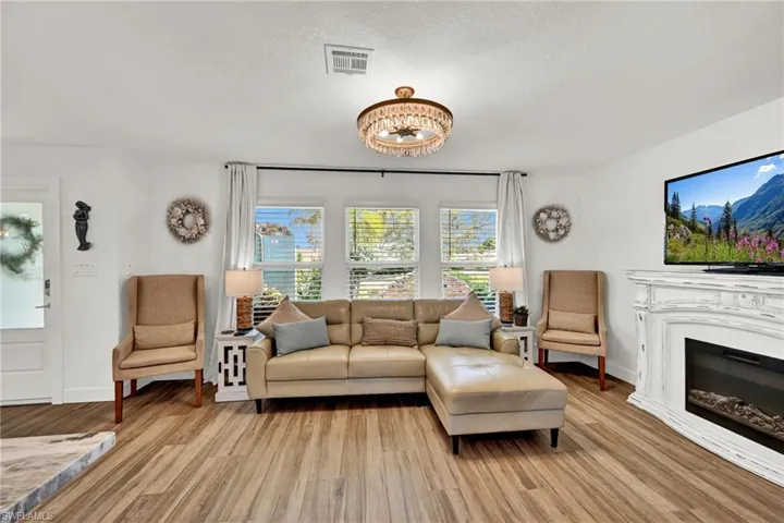 Living area featuring visible vents, a textured ceiling, light wood-style flooring, and a chandelier, electric fireplace, beautiful sunrises thru the front windows