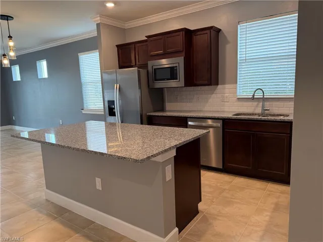 Kitchen featuring light stone counters, stainless steel appliances, sink, decorative light fixtures, and a center island
