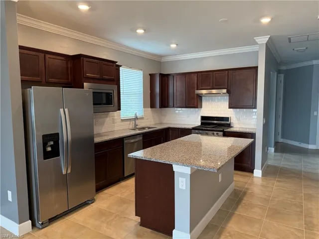 Kitchen with a center island, sink, light stone countertops, light tile patterned floors, and stainless steel appliances