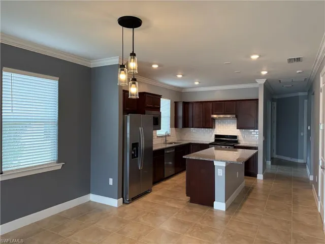 Kitchen with a center island, sink, stainless steel appliances, tasteful backsplash, and light stone counters