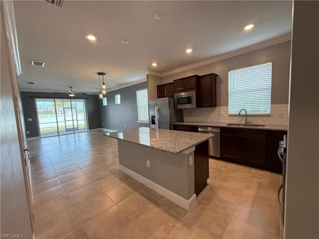 Kitchen with a center island, sink, ceiling fan, light stone counters, and stainless steel appliances