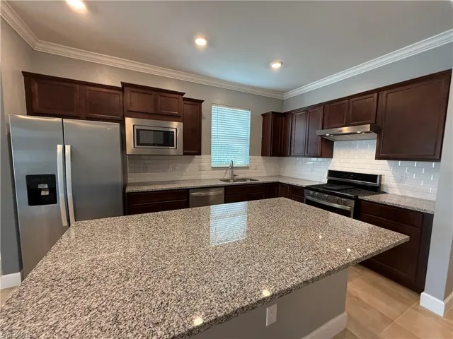 Kitchen with sink, light stone countertops, light tile patterned floors, tasteful backsplash, and stainless steel appliances