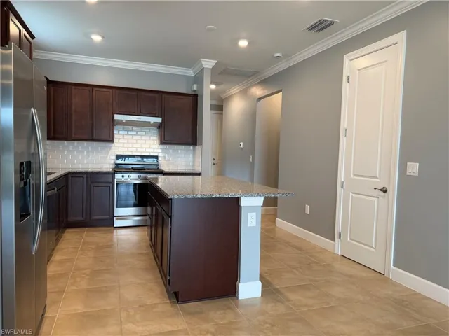 Kitchen featuring light stone countertops, a center island, stainless steel appliances, decorative backsplash, and light tile patterned floors