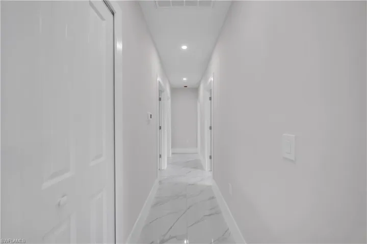 Recessed ceiling lighting illuminates a hallway with white walls and a large format tile floor