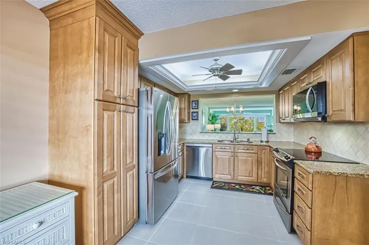 Kitchen with appliances with stainless steel finishes, light stone counters, a tray ceiling, light tile patterned floors, and brown cabinetry
