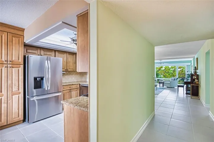 Kitchen featuring a textured ceiling, stainless steel fridge, light tile patterned floors, ceiling fan, and decorative backsplash