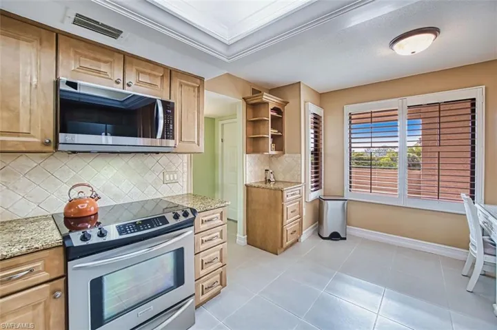 Kitchen featuring stainless steel appliances, light stone countertops, open shelves, backsplash, and light tile patterned flooring