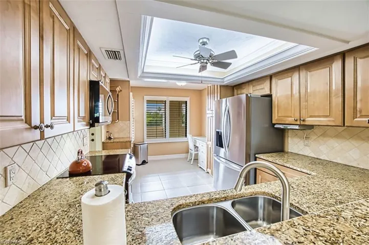 Kitchen featuring backsplash, appliances with stainless steel finishes, light stone counters, and a tray ceiling