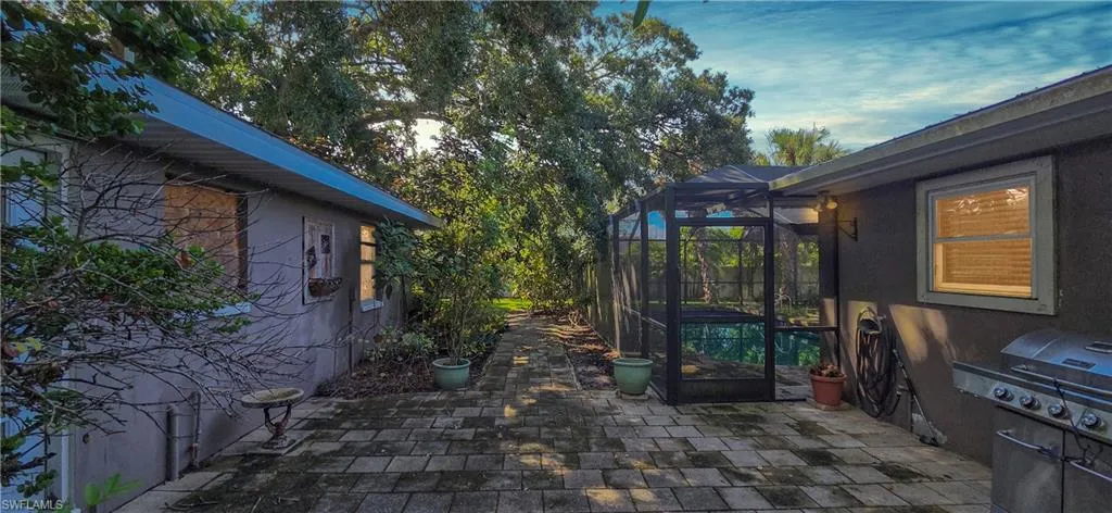 Paved patio area featuring a screened pool enclosure and mature trees