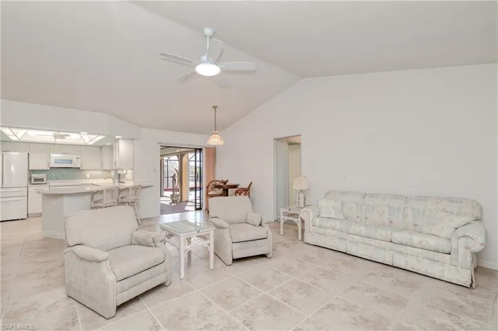 Living room with ceiling fan, light tile patterned flooring, and vaulted ceiling