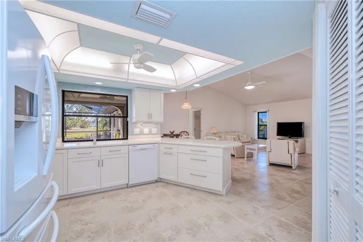 Kitchen with white appliances, kitchen peninsula, hanging light fixtures, ceiling fan, and white cabinetry