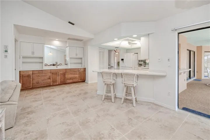 Kitchen with lofted ceiling, white refrigerator with ice dispenser, white cabinets, a kitchen breakfast bar, and kitchen peninsula