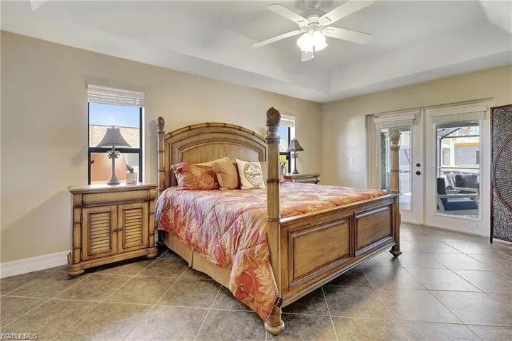 Tiled bedroom featuring access to exterior, a tray ceiling, and a ceiling fan