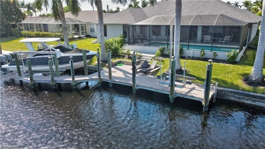 Dock featuring a water view, boat lift, a yard, a sunroom, and a lanai