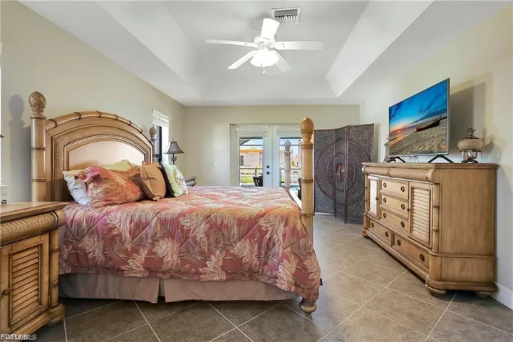 Tiled bedroom featuring french doors, access to exterior, a ceiling fan, and a tray ceiling