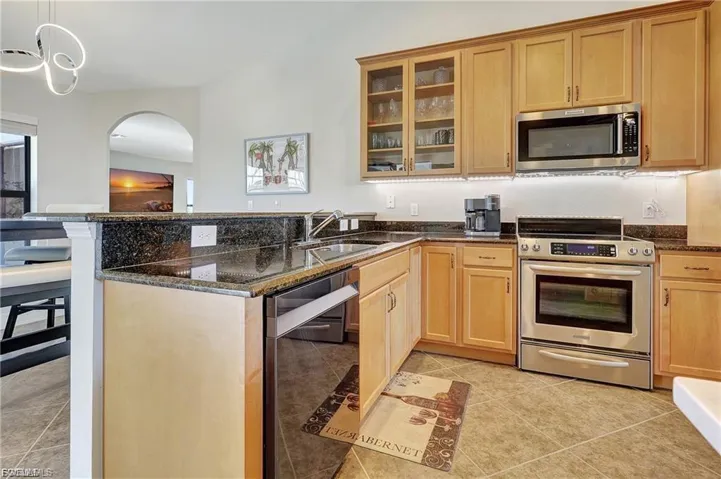 Kitchen featuring a peninsula, stainless steel appliances, glass fronted cabinets, dark stone countertops, and hanging light fixtures