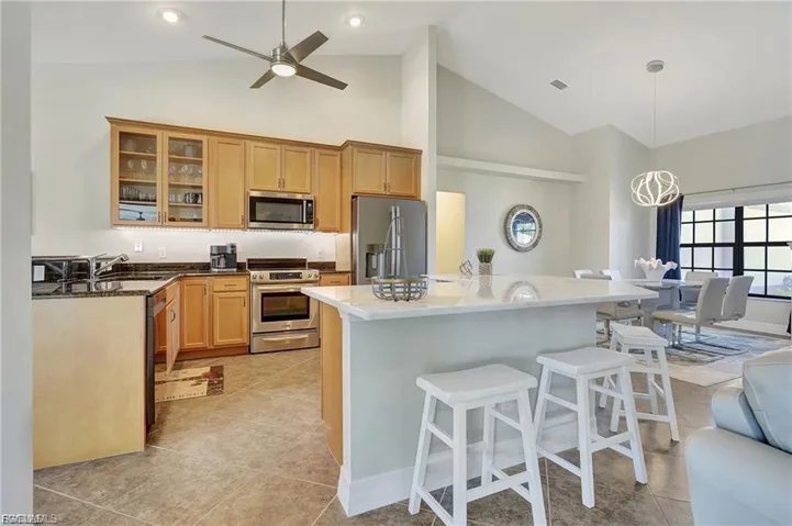 Kitchen with dark stone countertops, glass insert cabinets, stainless steel appliances, a kitchen island, and lofted ceiling