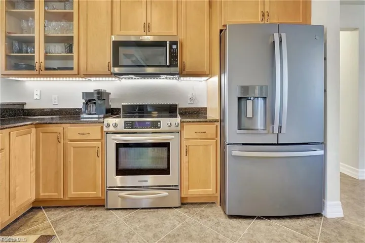 Kitchen featuring stainless steel appliances, dark stone counters, glass fronted cabinets, and light wood finish cabinets