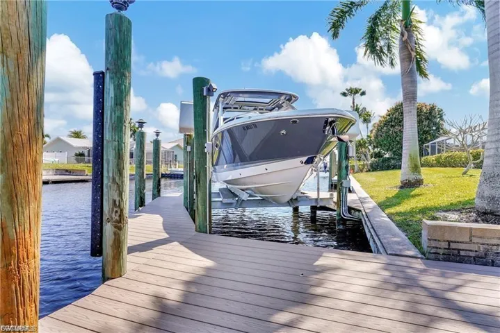 Dock area with boat lift, a water view, and a yard