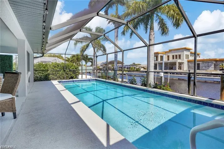 Outdoor pool featuring a sunroom, a water view, glass enclosure, and a patio area