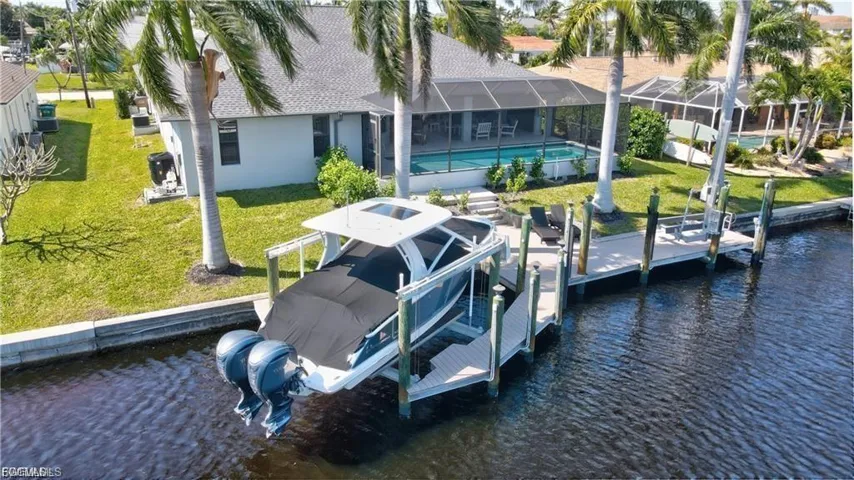 Dock featuring boat lift, a water view, a yard, and an outdoor pool