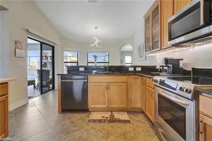 Kitchen with stainless steel appliances, decorative light fixtures, glass fronted cabinets, dark stone countertops, and light tile patterned flooring