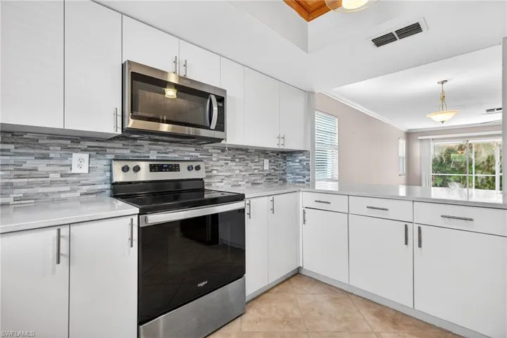Kitchen with stainless steel appliances, crown molding, white cabinetry, hanging light fixtures, and light tile patterned floors