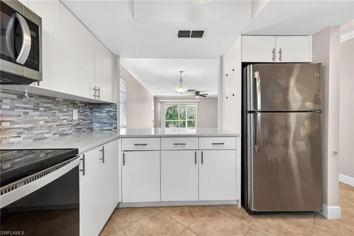 Kitchen with appliances with stainless steel finishes, white cabinetry, decorative backsplash, ornamental molding, and light stone countertops