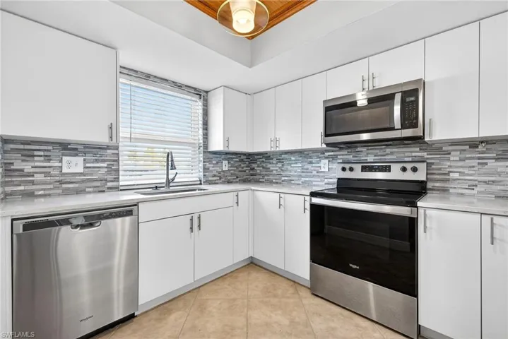 Kitchen featuring appliances with stainless steel finishes, white cabinetry, light tile patterned flooring, and light stone counters