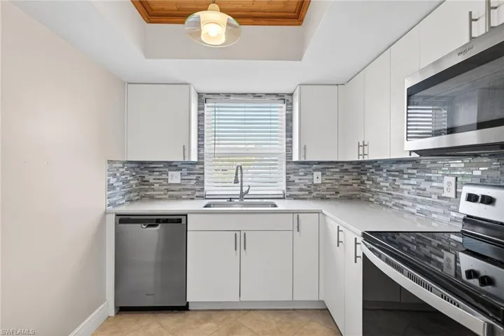Kitchen with appliances with stainless steel finishes, white cabinetry, light tile patterned floors, tasteful backsplash, and a raised ceiling