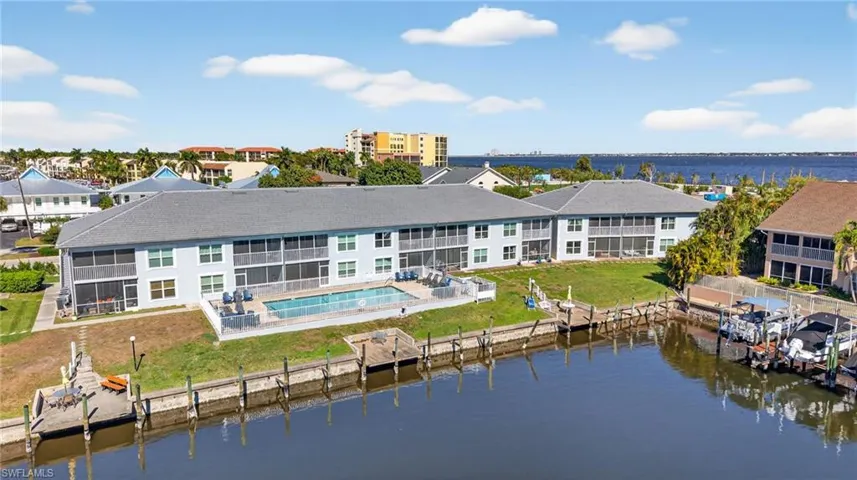 Back of property featuring a community pool, a water view, a patio area, and a lawn