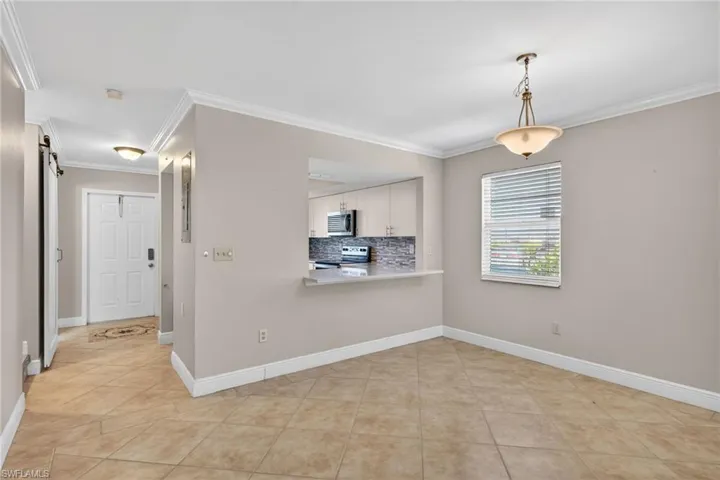 Kitchen with light countertops, crown molding, hanging light fixtures, decorative backsplash, and appliances with stainless steel finishes