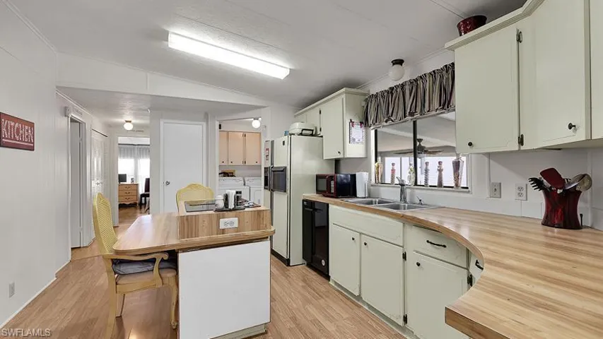 Kitchen with light countertops, vaulted ceiling, black dishwasher, white fridge with ice dispenser, and light wood-style floors