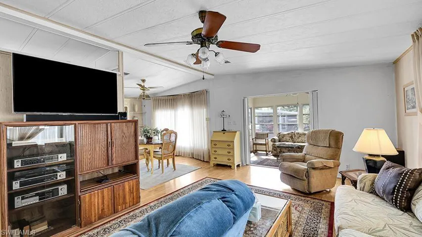 Living area with ceiling fan, wood finished floors, and vaulted ceiling with beams