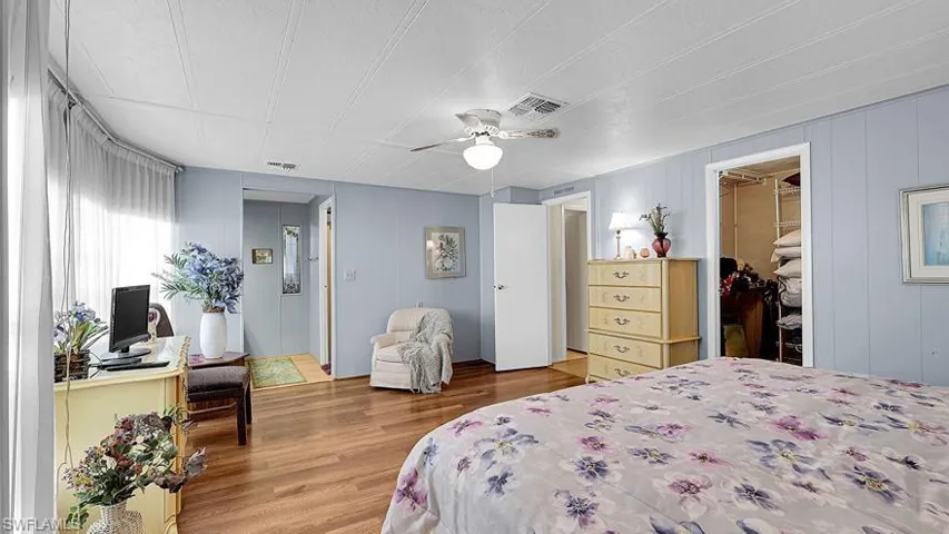 Bedroom featuring a walk in closet, wood finished floors, a ceiling fan, and wood walls