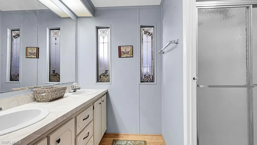 Full bathroom featuring double vanity, a shower stall, and light wood-type flooring
