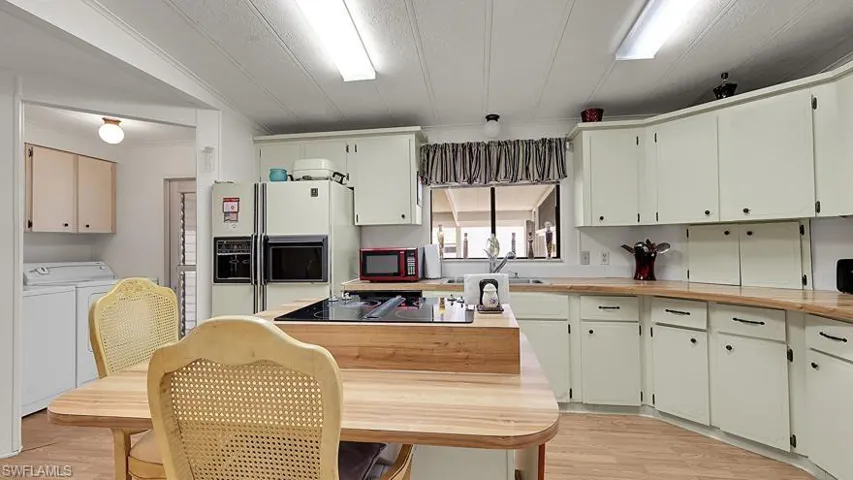 Kitchen featuring white fridge with ice dispenser, light wood-style floors, washing machine and clothes dryer, butcher block counters, and black electric stovetop