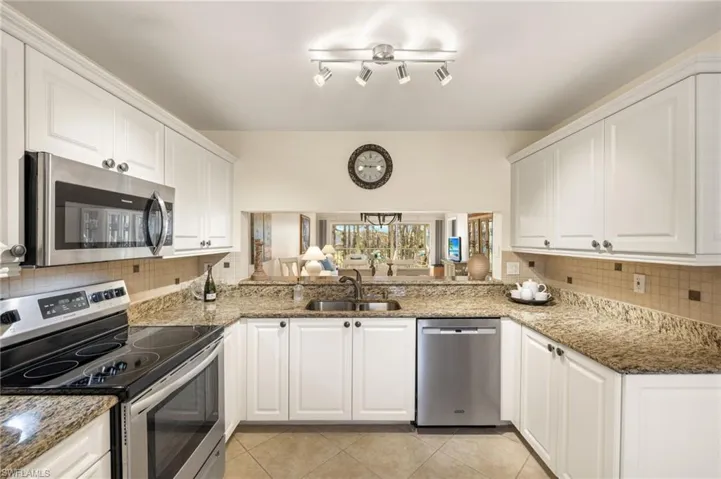 Kitchen with appliances with stainless steel finishes, white cabinetry, sink, dark stone countertops, and light tile patterned floors