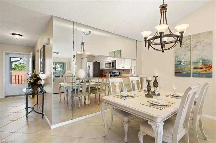 Tiled dining area featuring lofted ceiling, a notable chandelier, and a textured ceiling