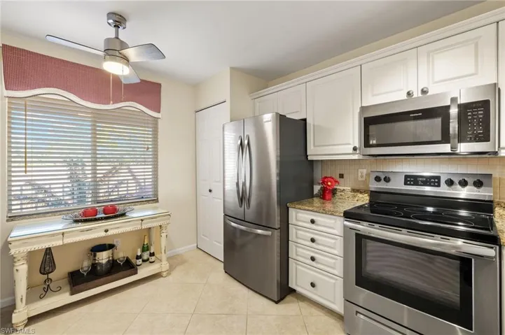 Kitchen with light tile patterned floors, white cabinetry, stainless steel appliances, decorative backsplash, and dark stone counters