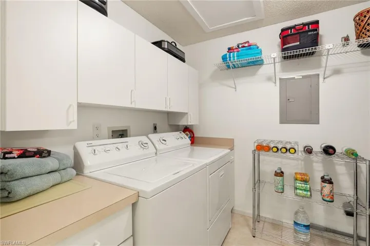 Clothes washing area with cabinets, electric panel, and washer and clothes dryer