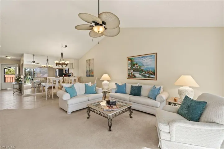 Carpeted living room featuring ceiling fan with notable chandelier and high vaulted ceiling