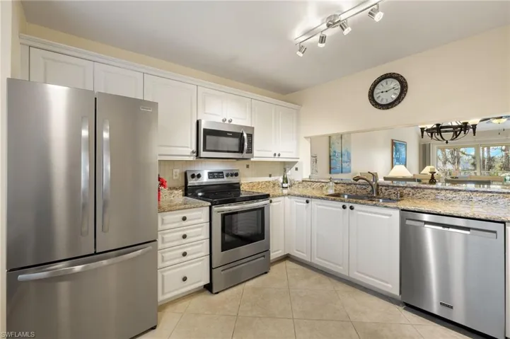 Kitchen with appliances with stainless steel finishes, sink, white cabinets, light tile patterned floors, and light stone counters