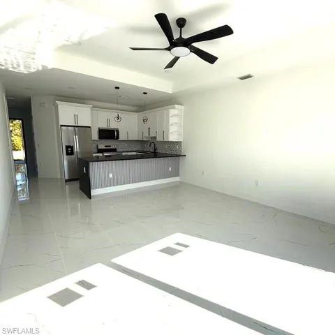 Kitchen featuring white cabinetry, open floor plan, stainless steel appliances, decorative light fixtures, and light marble finish flooring
