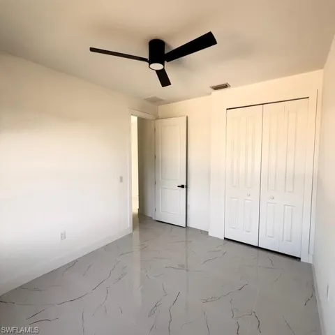 Unfurnished bedroom featuring light marble finish flooring, ceiling fan, and a closet